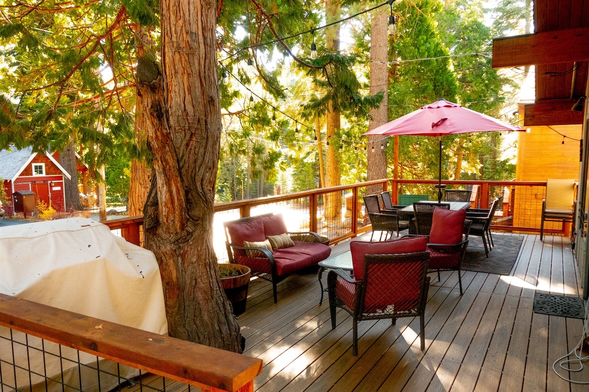 Large tree-shaded deck with outdoor lounge seating and dining space.